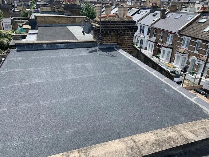 Aerial view of a flat roof with gray tar coating, surrounded by brick townhouses and adjacent buildings in an urban residential area