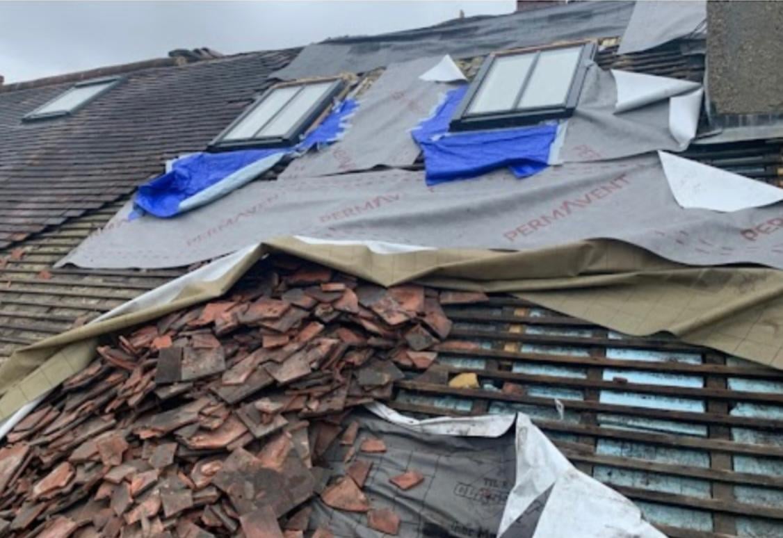 Roof under repair with removed clay tiles, exposed battens, protective tarps, and blue skylights during renovation work