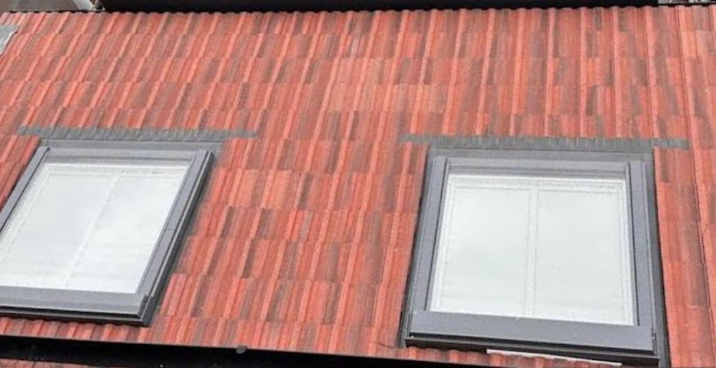 Two skylight windows with gray frames installed on a red corrugated metal roof